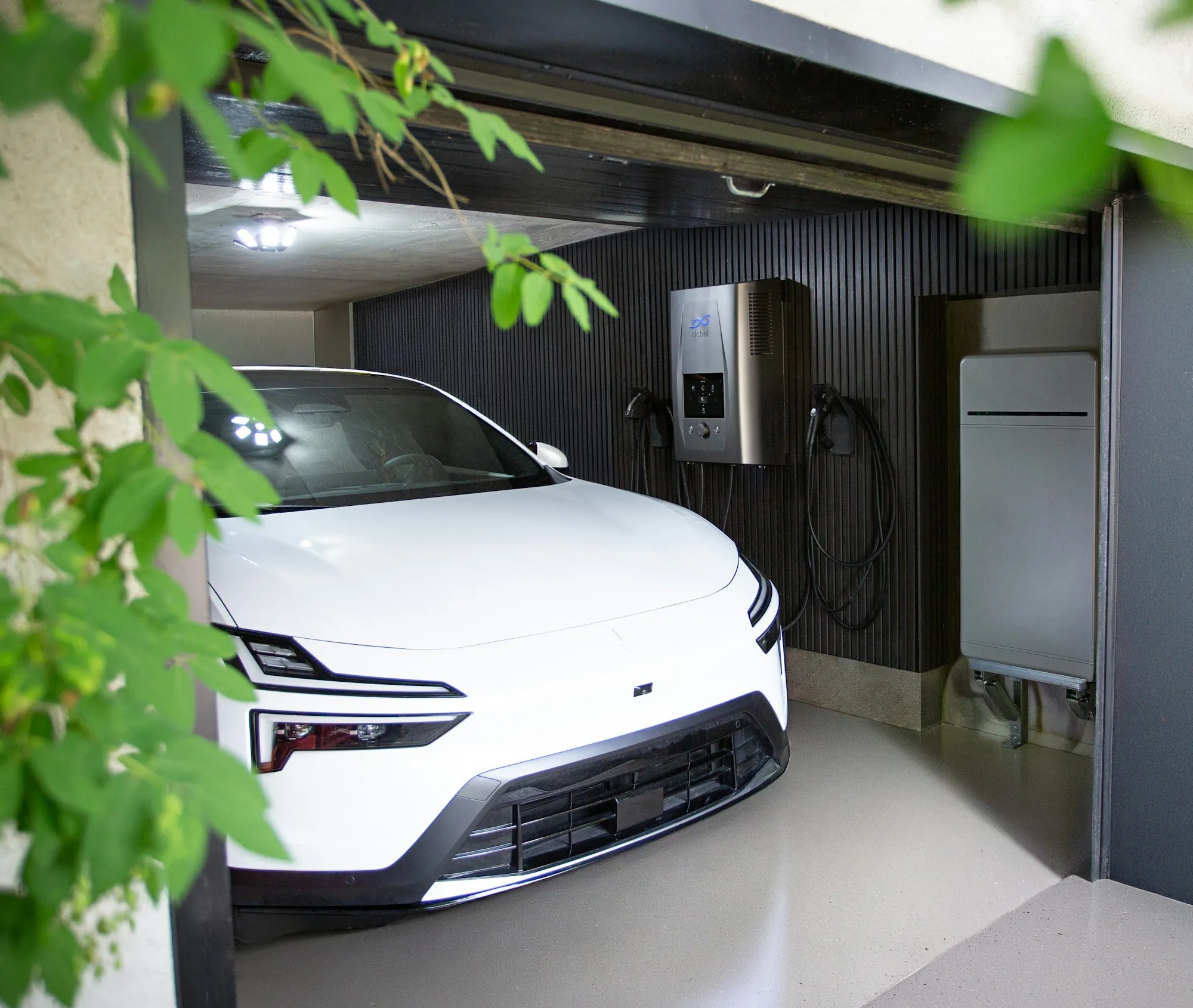 A white electric car in a garage beside a wall-mounted charging station